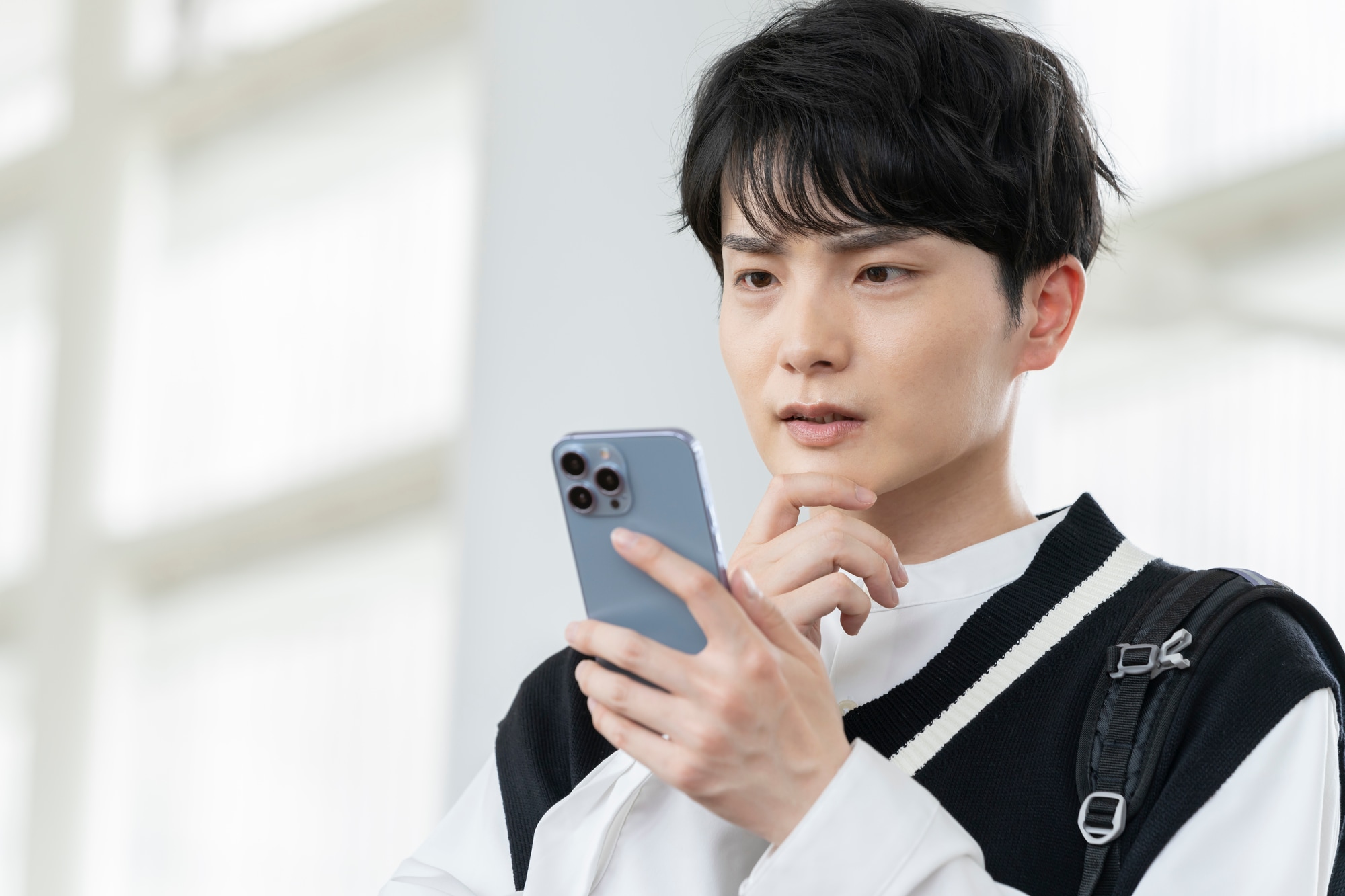 スマートフォンを見ながら考え込む男性