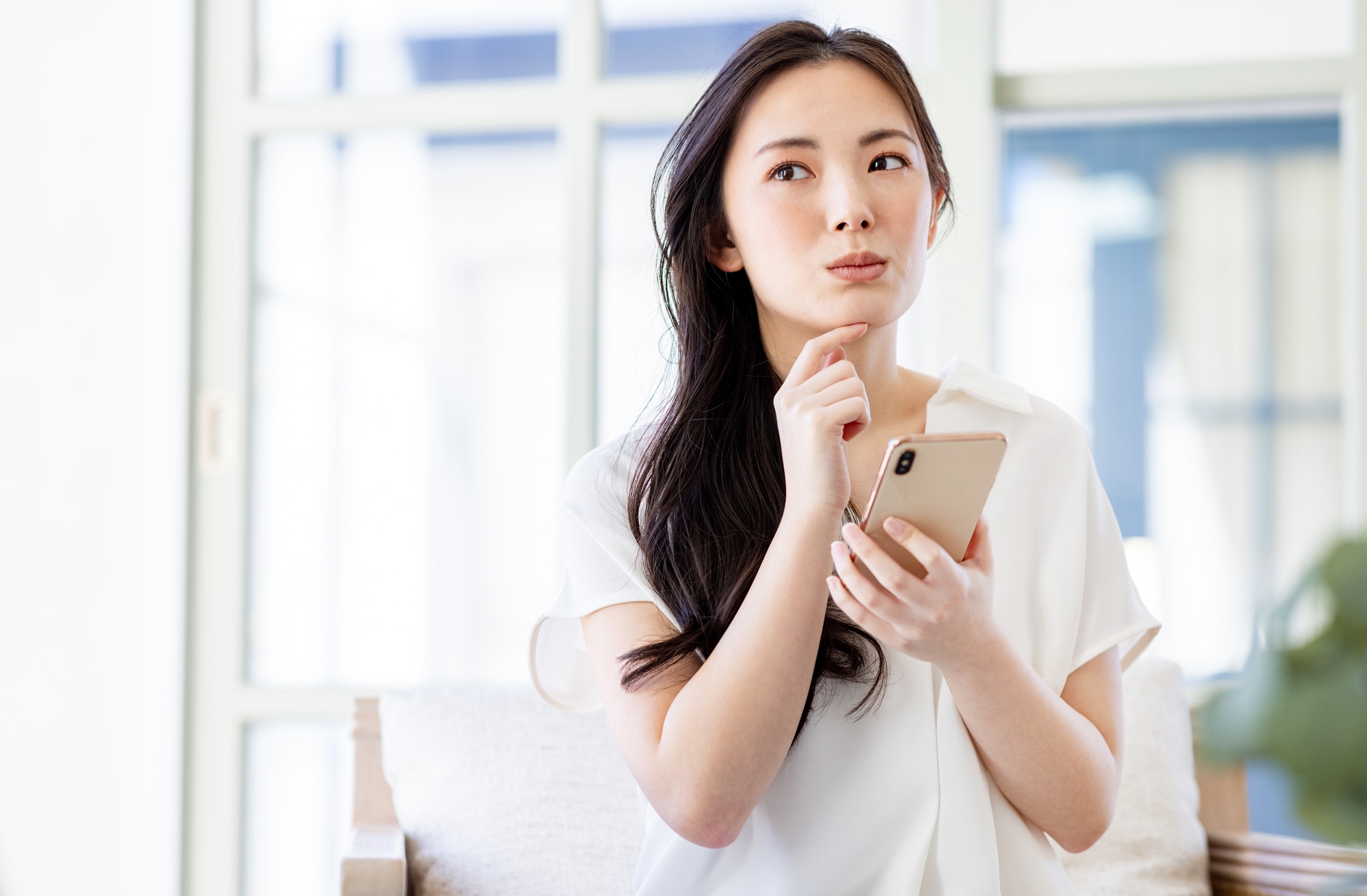 スマホを片手に考える女性