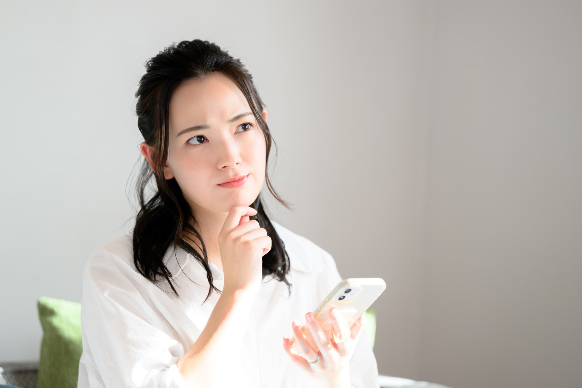 スマートフォンを持って考える女性