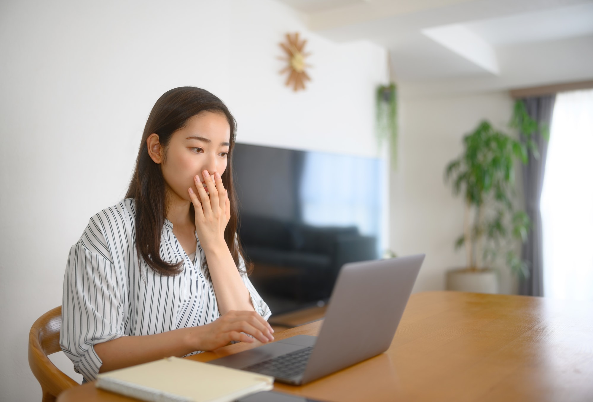 ノートパソコンを見て口に手を当てて驚く女性