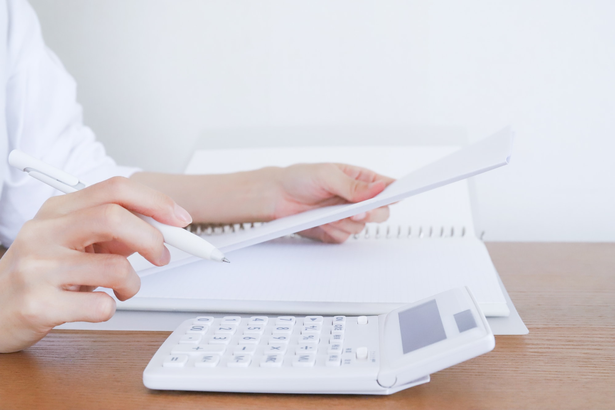 机に電卓を置きペンと紙を持つ手元
