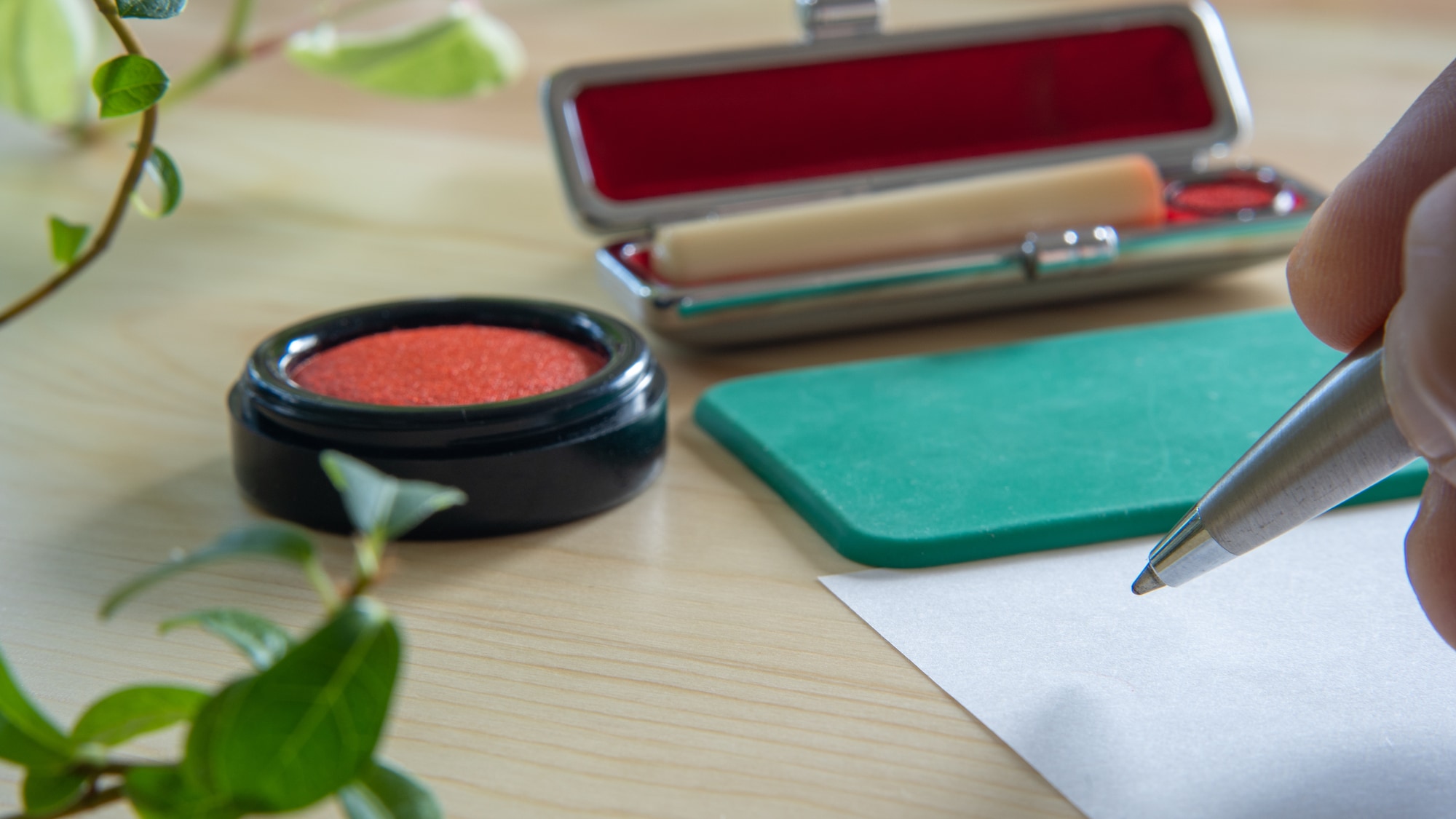 朱肉と印鑑の近くに置かれた書類に署名する手元