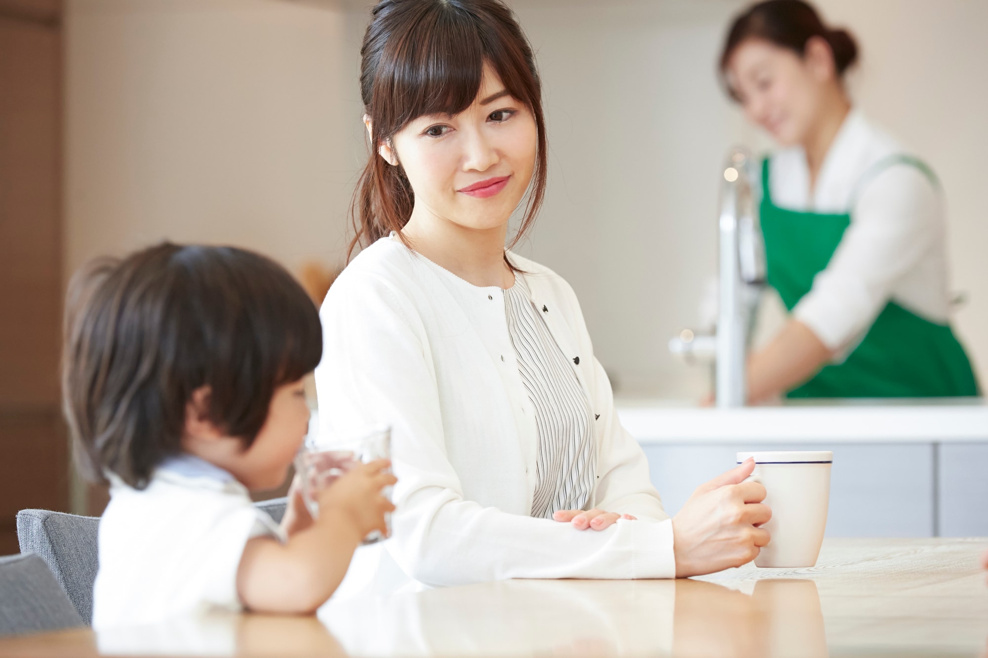 キッチンで家事をする女性と座っている母親と子供