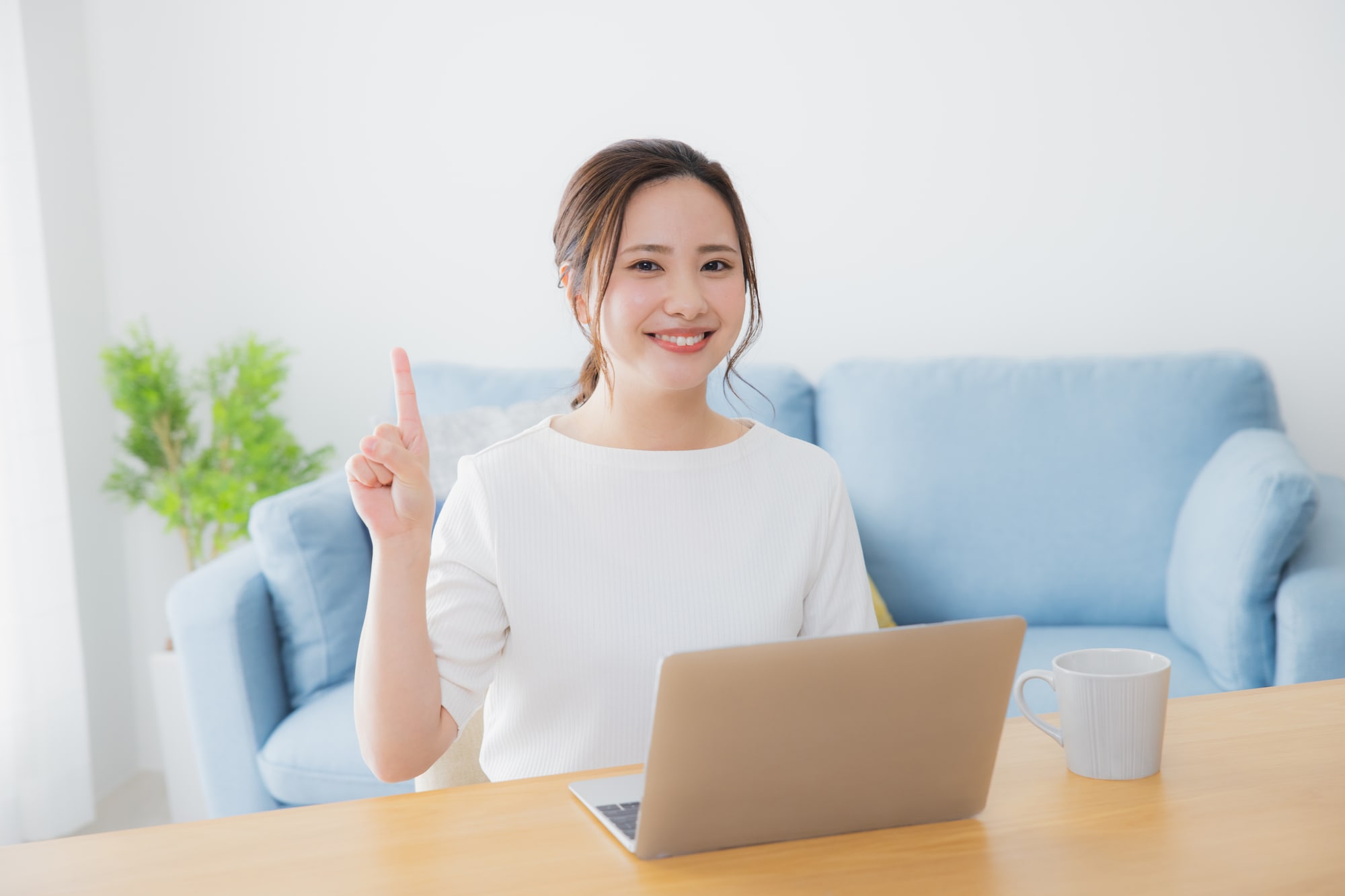 パソコンの前で人差し指を立てて笑顔な女性